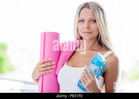 Jeune femme blonde passe fitness sport avec une serviette, une bouteille d'eau et rose tapis de yoga Banque D'Images