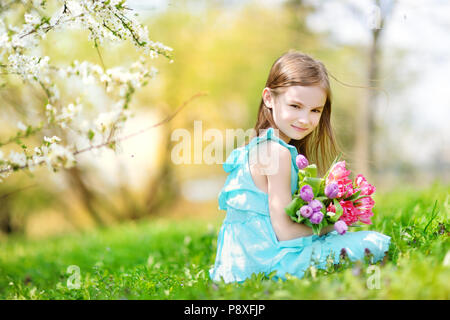 Adorable petite fille holding tulipes pour sa mère dans blooming cherry garden sur beau jour de printemps Banque D'Images