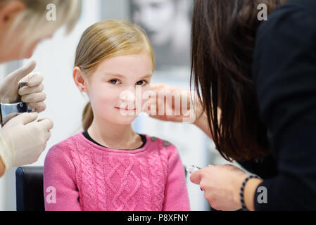 Adorable petite fille ayant le perçage des oreilles processus avec équipement spécial dans le centre de beauté par un professionnel de la santé Banque D'Images