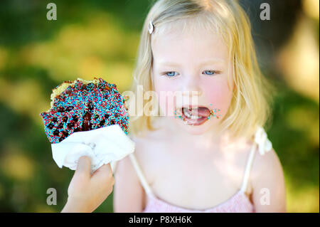 Little girl eating gaufre belge sur un bâton à l'extérieur sur chaude journée d'été Banque D'Images