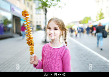 Cute little girl eating poêlée de pomme de terre sur un bâton sur chaude journée d'été en plein air Banque D'Images