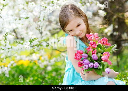 Adorable petite fille holding tulipes pour sa mère dans blooming cherry garden sur beau jour de printemps Banque D'Images