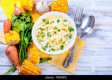 Soupe crème de maïs fait maison avec de la crème, les herbes dans une assiette blanche et des tranches d'épis de maïs frit sur une table en bois blanc. Vue de dessus, copy space Banque D'Images