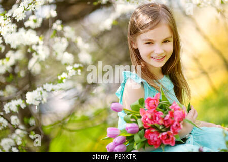 Adorable petite fille holding tulipes pour sa mère dans blooming cherry garden sur beau jour de printemps Banque D'Images