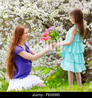 Adorable petite fille remise de tulipes sa mère dans blooming cherry garden sur beau jour de printemps Banque D'Images