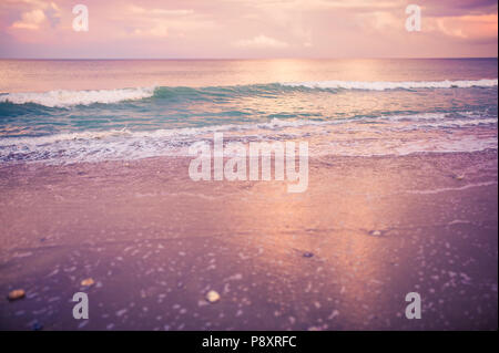 Rose, violet, rose et or crépuscule coucher de soleil sur la plage avec un sable teinté de rose et d'une rive de gros plan détaillé, les vagues de l'océan bleu turquoise brillant Banque D'Images