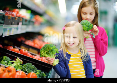 Deux mignonnes petites sœurs choisissant le brocoli frais dans un magasin d'alimentation ou d'un supermarché Banque D'Images