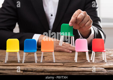 La main d'affaires prendre fauteuil vert entre autres sur un bureau en bois Banque D'Images