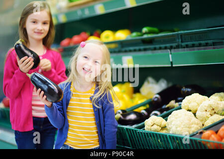 Deux mignonnes petites soeurs de choisir des aubergines dans un magasin d'alimentation ou d'un supermarché Banque D'Images