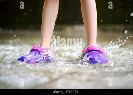 Enfant portant des chaussures en caoutchouc de sauter dans une flaque d'eau sur chaude journée d'été Banque D'Images