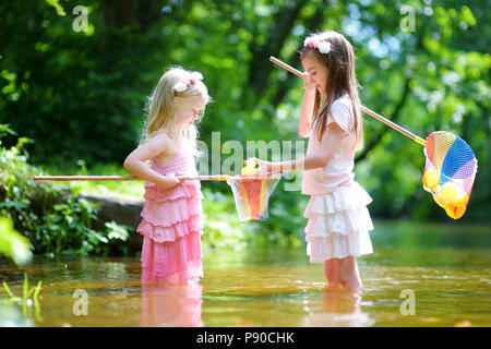 Deux mignonnes petites sœurs jouant dans une rivière capture de canards en caoutchouc avec leur scoop-filets de jour d'été chaud et ensoleillé Banque D'Images