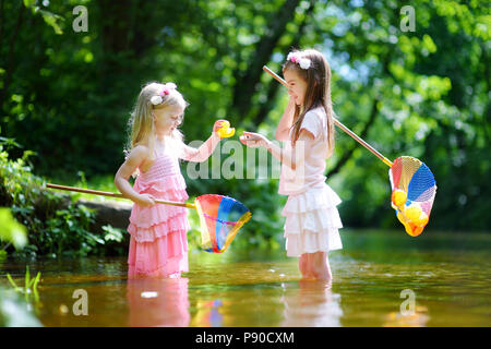 Deux mignonnes petites sœurs jouant dans une rivière capture de canards en caoutchouc avec leur scoop-filets de jour d'été chaud et ensoleillé Banque D'Images