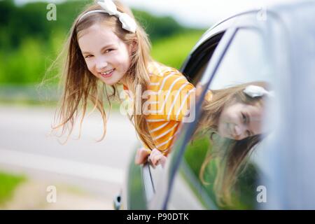 Funny little girl est bloqué sa tête hors de la fenêtre de la voiture à l'avant pour un roadtrip ou voyager Banque D'Images