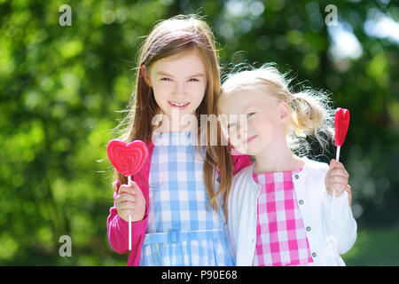 Deux mignonnes petites sœurs de manger des sucettes en forme de cœur à l'extérieur sur beau jour d'été Banque D'Images