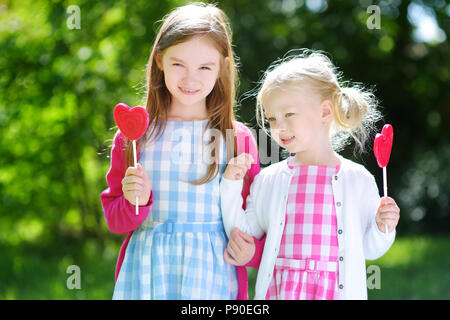 Deux mignonnes petites sœurs de manger des sucettes en forme de cœur à l'extérieur sur beau jour d'été Banque D'Images