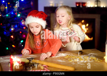 Deux adorables petites soeurs baking Christmas cookies par une cheminée la veille de Noël Banque D'Images