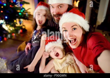 Famille de quatre jeunes heureux de prendre une photo d'eux-mêmes par une cheminée dans un confortable salon sombre la veille de Noël Banque D'Images