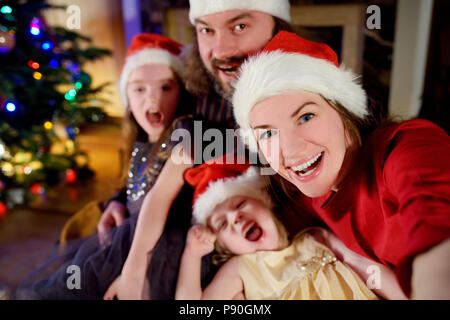 Famille de quatre jeunes heureux de prendre une photo d'eux-mêmes par une cheminée dans un confortable salon sombre la veille de Noël Banque D'Images