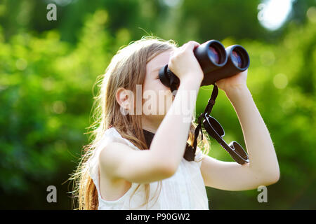 Funny little girl looking through binoculars aux beaux jours d'été Banque D'Images