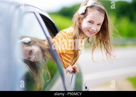 Funny little girl est bloqué sa tête hors de la fenêtre de la voiture à l'avant pour un roadtrip ou voyager Banque D'Images