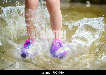 Enfant portant des chaussures en caoutchouc de sauter dans une flaque d'eau sur chaude journée d'été Banque D'Images