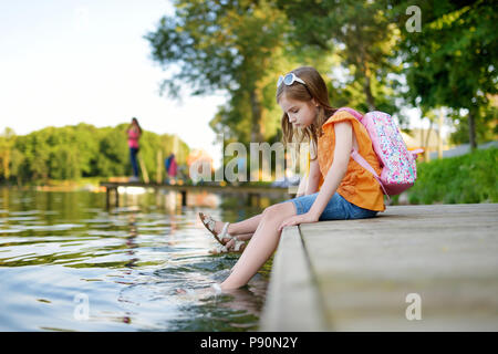 Deux mignonnes petites filles assis sur une plate-forme de bois par la rivière ou lac trempant leurs pieds dans l'eau chaude journée d'été sur Banque D'Images