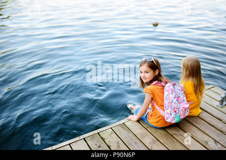 Deux mignonnes petites filles assis sur une plate-forme de bois par la rivière ou lac trempant leurs pieds dans l'eau chaude journée d'été sur Banque D'Images