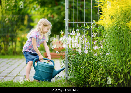 Cute little girl arrosage des fleurs dans le jardin de l'été jour Banque D'Images