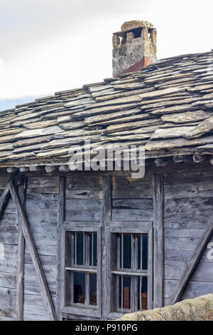 Deux petites fenêtres dans le mur d'une vieille maison de bois avec plaque en pierre et la cheminée de toit en Bulgarie Banque D'Images