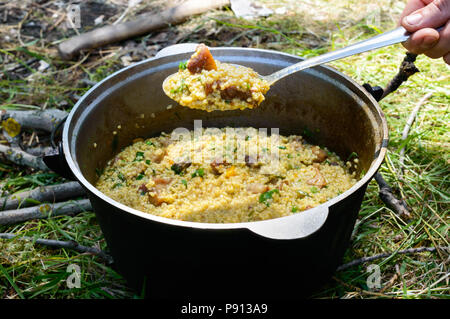 Porridge délicieux couscous avec de la viande, des légumes et des herbes fraîches dans une casserole cuisson sur la nature. Banque D'Images