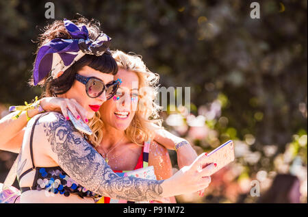 Deux femmes festivaliers en robes colorées, en tenant un smartphone, en utilisant selfies, à une latitude Festival, Henham Park, Suffolk, Angleterre, 14 juillet 2018 Banque D'Images