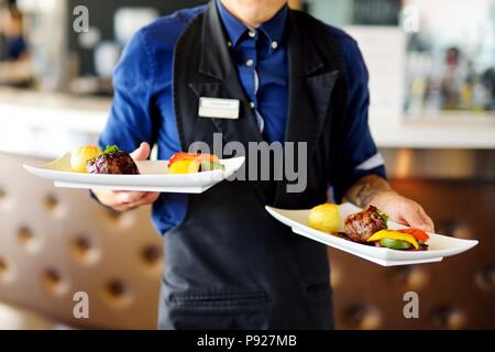 Waiter carrying deux plaques avec plat de viande sur certains événement festif, parti, réception de mariage ou événement Banque D'Images