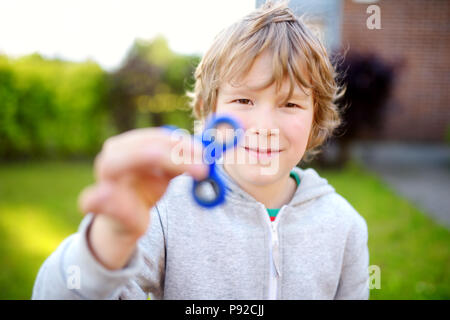 Cute school boy playing with colorful fidget spinner sur l'aire de jeux. Populaires jouet anti-stress pour l'école les enfants et les adultes. Banque D'Images