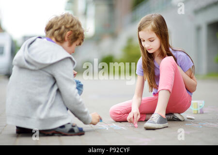 Deux heureux enfants dessiner avec les craies colorées sur un trottoir. L'activité d'été pour les petits enfants. Loisirs créatifs pour la famille. Banque D'Images