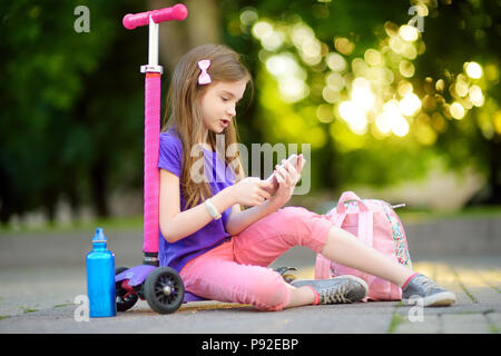 Petit enfant apprendre à conduire un scooter dans un parc de la ville par beau soir d'été. Cute little girl riding d'un rouleau. Des loisirs actifs et le sport de plein air pour Banque D'Images