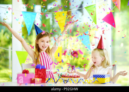 Deux petites soeurs ayant d'anniversaire à la maison, souffler les bougies sur le gâteau d'anniversaire. Kids Birthday party avec décorations colorées, des cadeaux et de l'interdiction Banque D'Images