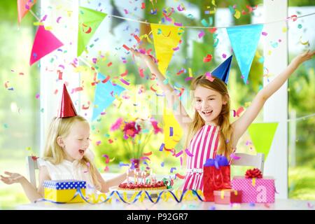 Deux petites soeurs ayant d'anniversaire à la maison, souffler les bougies sur le gâteau d'anniversaire. Kids Birthday party avec décorations colorées, des cadeaux et de l'interdiction Banque D'Images