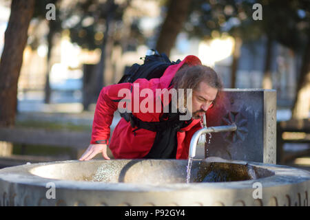 L'homme de boire de l'eau minérale à partir de la ville fontaine dans Mestia village sur chilly journée ensoleillée à la fin de l'automne. Paysage de montagne Haut Svaneti regio Banque D'Images