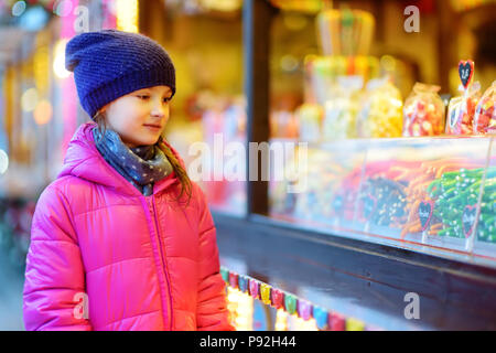 Cute little girl le choix des bonbons sur le marché de Noël traditionnel pour les froides journée d'hiver. L'achat des bonbons et biscuits pour enfants le jour de Noël. Banque D'Images