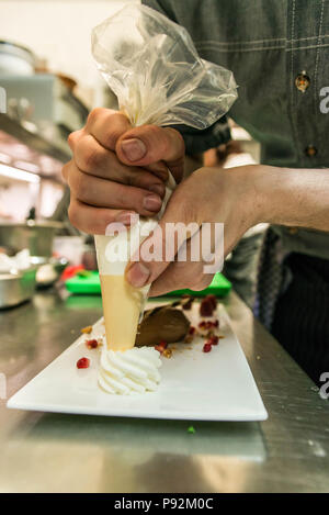 Faire cuire la crème à l'ajout d'un morceau de mousse de marron au chocolat dessert sucré et décoration sur une plaque blanche background Banque D'Images