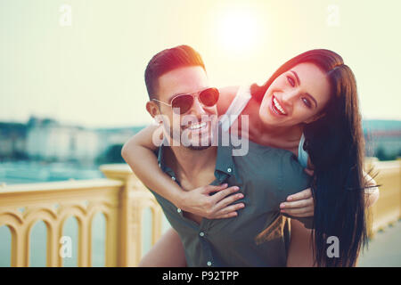 Couple heureux à l'extérieur dans le coucher du soleil, ville femme piggyback Banque D'Images