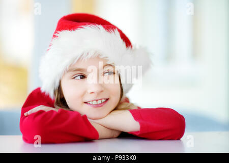 Adorable little girl wearing Santa hat le matin de Noël. La célébration de Noël à la maison. Banque D'Images