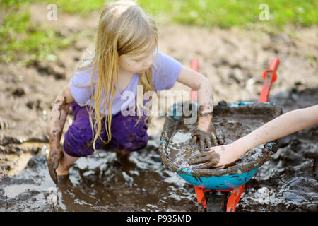 Funny little girl playing dans une grande flaque de boue humide par beau jour d'été. Enfant de se salir en creusant dans le sol boueux. Jeux en plein air. malpropre Banque D'Images