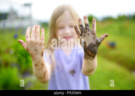 Funny little girl playing dans une grande flaque de boue humide par beau jour d'été. Enfant de se salir en creusant dans le sol boueux. Jeux en plein air. malpropre Banque D'Images