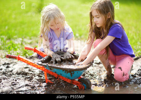 Deux drôles de petites filles jouant dans une grande flaque de boue humide par beau jour d'été. Les enfants se salir en creusant dans le sol boueux. Jeux en plein air en désordre Banque D'Images