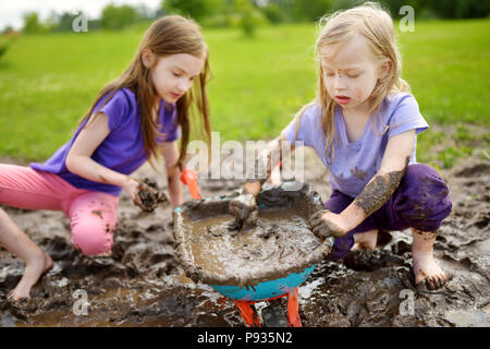 Deux drôles de petites filles jouant dans une grande flaque de boue humide par beau jour d'été. Les enfants se salir en creusant dans le sol boueux. Jeux en plein air en désordre Banque D'Images