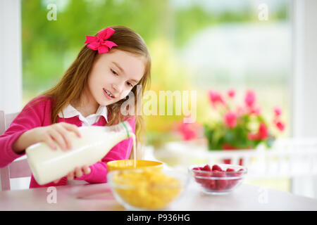 Cute little girl en compagnie de ses hôtes à la maison. Jolie enfant de manger les flocons de maïs et les framboises et boire du lait avant l'école. La nutrition saine fo Banque D'Images