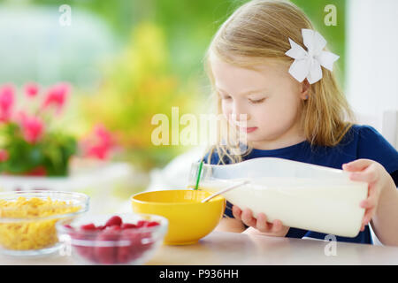 Cute little girl en compagnie de ses hôtes à la maison. Jolie enfant de manger les flocons de maïs et les framboises et boire du lait avant l'école. La nutrition saine fo Banque D'Images