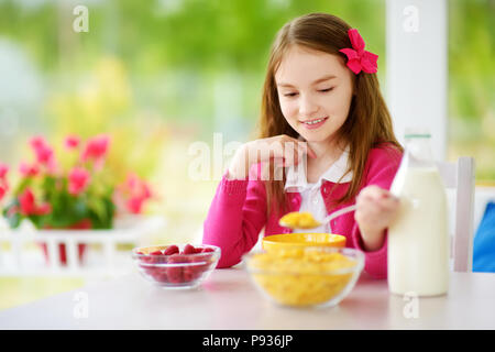 Cute little girl en compagnie de ses hôtes à la maison. Jolie enfant de manger les flocons de maïs et les framboises et boire du lait avant l'école. La nutrition saine fo Banque D'Images