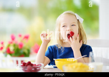 Cute little girl en compagnie de ses hôtes à la maison. Jolie enfant de manger les flocons de maïs et les framboises et boire du lait avant l'école. La nutrition saine fo Banque D'Images